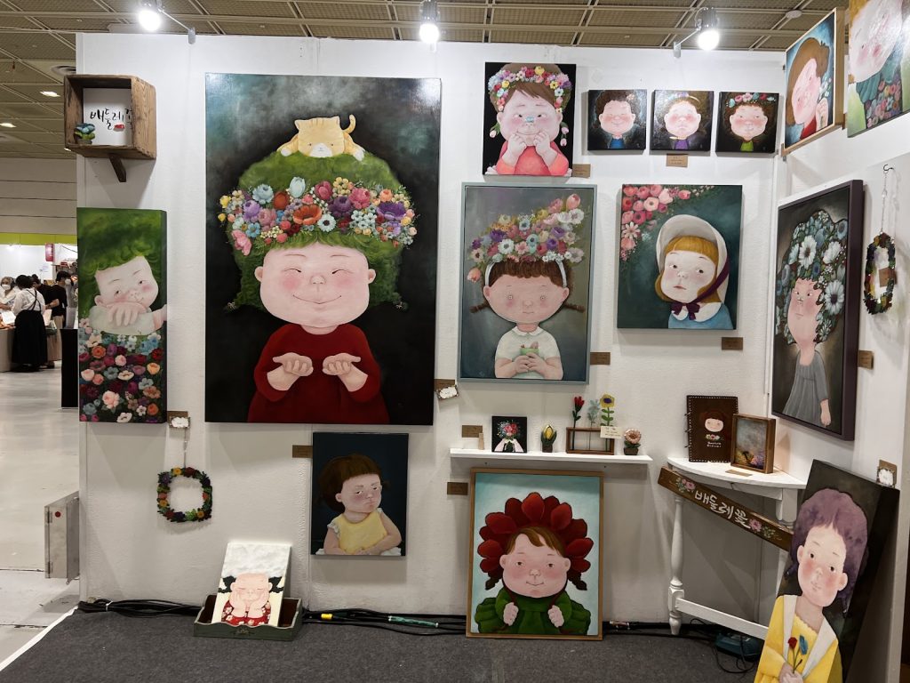 Original paintings and whimsical artwork displayed at an artist's booth.