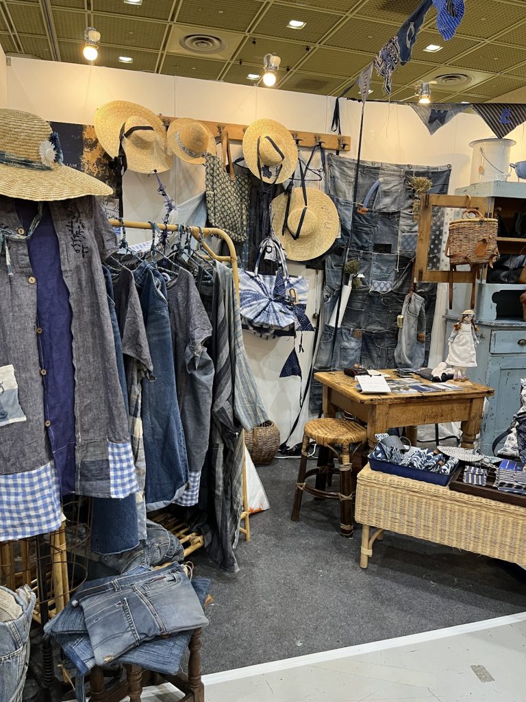 Handcrafted clothing, hats, bags, and indigo textiles displayed by an artisan vendor.