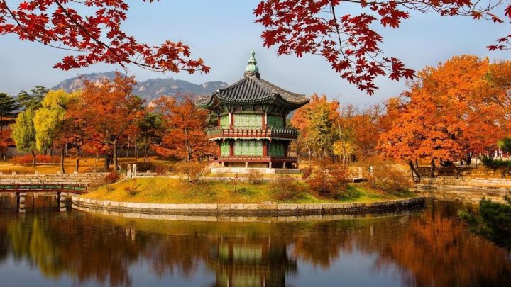 Traditional Korean pavilion surrounded by colorful red, orange, and yellow autumn foliage reflected in a pond