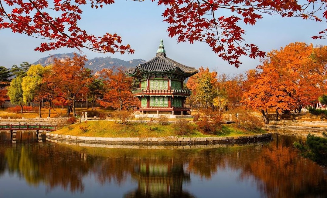 Traditional Korean pavilion surrounded by colorful red, orange, and yellow autumn foliage reflected in a pond